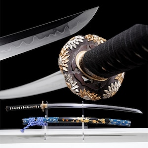 Peut inclure: Un katana japonais avec une lame incurvée et un motif floral complexe sur la garde. Le manche est enveloppé de tissu noir et le fourreau est bleu avec des accents dorés. La lame est exposée sur un support transparent sur fond noir.
