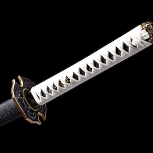 Puede incluir: Una espada katana japonesa con un mango blanco envuelto en un patr&oacute;n de diamantes. La guarda es negra y dorada, y la hoja es negra. La espada est&aacute; sobre un fondo negro.