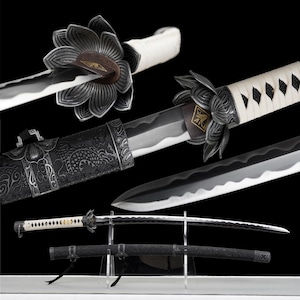 Pode incluir: Uma variedade de espadas katana japonesas. As espadas apresentam tsubas ornamentadas em forma de flor, cabos brancos enrolados e bainhas pretas. As lâminas são prateadas e pretas, e os cabos são brancos. As bainhas são pretas com desenhos intrincados.