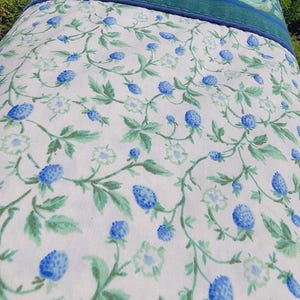 May include: A floral patterned pillowcase featuring a white background with blue berry and green leaf designs. The top border is a solid teal green with a thin blue trim. The pillowcase is likely made of cotton or a similar fabric.
