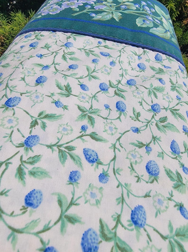 May include: A floral patterned pillowcase featuring a white background with blue berry and green leaf designs. The top border is a solid teal green with a thin blue trim. The pillowcase is likely made of cotton or a similar fabric.