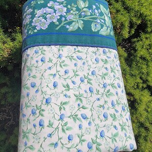 May include: A pillowcase with a floral design. The top portion is teal with a floral pattern in shades of blue and green. The bottom portion is white with a pattern of blue berries and green leaves.
