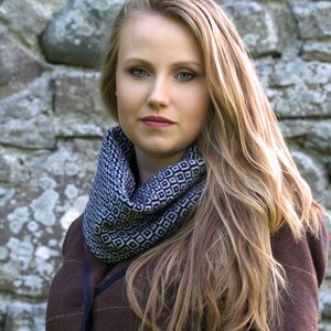 Pode incluir: Uma mulher com cabelo loiro comprido vestindo uma jaqueta de tweed marrom com um cachecol estampado em preto e branco. A jaqueta tem um padrão xadrez e um fecho de botão.