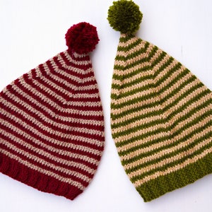 Puede incluir: Dos gorros de punto a rayas con pompones. Un gorro es rojo y blanco, el otro es verde y beige.