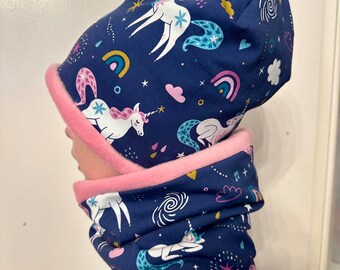 May include: A blue fleece hat and neck warmer with a unicorn, rainbow, and star pattern. The hat has a pink fleece lining.