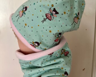 May include: A mint green beanie and matching neck warmer set featuring a repeating pattern of small fairies with dark hair, pink skirts, and gold stars. Both items are lined with a soft, pale pink fabric, providing a layered look.