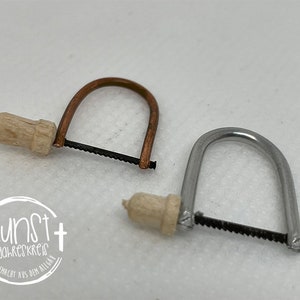 Op de afbeelding: Twee miniatuurzagen met houten handvatten. De zaag links heeft een koperen frame en de zaag rechts heeft een zilveren frame.