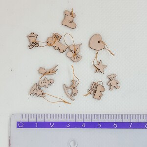 May include: A collection of 12 wooden ornaments in various shapes, including a star, heart, rocking horse, train, and a bell. The ornaments are all natural wood color and have a string attached for hanging.