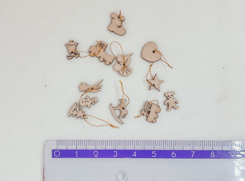 May include: A collection of 12 wooden ornaments in various shapes, including a star, heart, rocking horse, train, and a bell. The ornaments are all natural wood color and have a string attached for hanging.