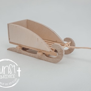 Può includere: Una slitta di legno con una finitura naturale e una corda attaccata. La slitta è vuota e pronta per un'avventura invernale.