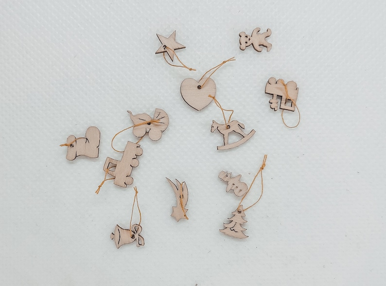 May include: A set of 12 wooden Christmas ornaments with a variety of shapes, including a star, a heart, a rocking horse, a truck, a bell, a snowman, a tree, and a few other abstract shapes. The ornaments are all made of natural wood and have a rustic, handmade look.