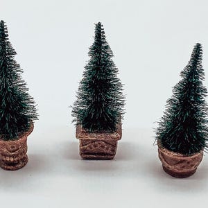 Peut inclure: Trois petits sapins de Noël artificiels dans des pots bruns. Les sapins sont verts et touffus.