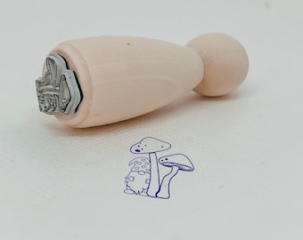 May include: A wooden stamp with a gray design of a mushroom with a white background. The stamp is shaped like a rounded rectangle with a round handle.