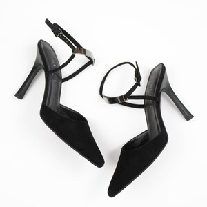 May include: A pair of black high-heeled sandals with pointed toes. The sandals have thin ankle straps with silver-toned metal accents and a buckle closure. The heels are slender and black.