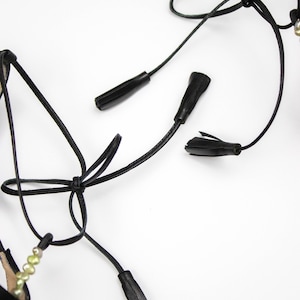 Puede incluir: Sandalias de cuero negro con correas para atar y borlas decorativas. Las sandalias presentan un dise&ntilde;o minimalista con un enfoque en los intrincados detalles de los lazos y adornos. La est&eacute;tica general es elegante y refinada.