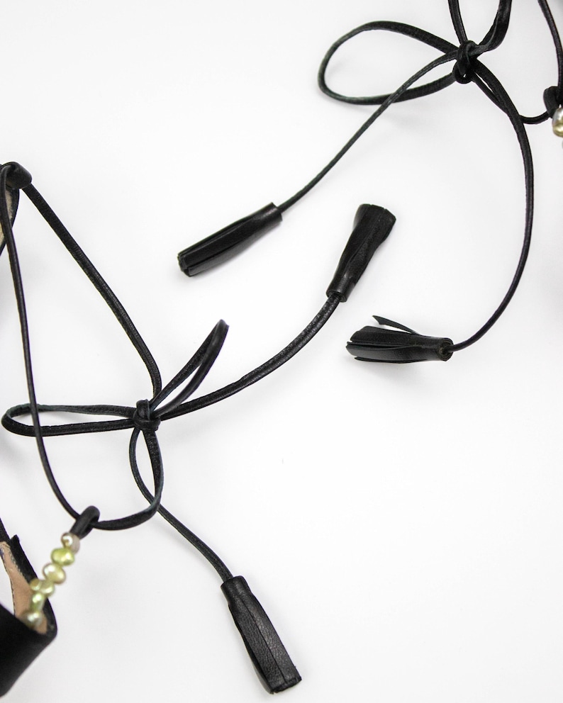 Puede incluir: Sandalias de cuero negro con correas para atar y borlas decorativas. Las sandalias presentan un dise&ntilde;o minimalista con un enfoque en los intrincados detalles de los lazos y adornos. La est&eacute;tica general es elegante y refinada.