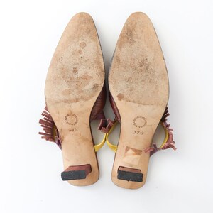 K&ouml;nnte beinhalten: Ein Paar braune Ledersandalen mit Absatz und gelben und burgunderfarbenen Fransenakzenten. Die Sandalen haben eine spitze Zehenpartie und einen kleinen Blockabsatz. Die Gr&ouml;&szlig;e 37 1/2 ist auf den Sohlen aufgedruckt.