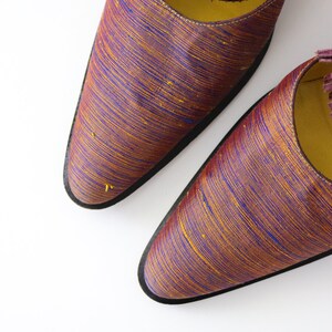 K&ouml;nnte beinhalten: Ein Paar spitze Schuhe mit einem Obermaterial aus burgunderfarbenem und goldenem gestreiftem Stoff. Die Schuhe haben eine schwarze Sohle.