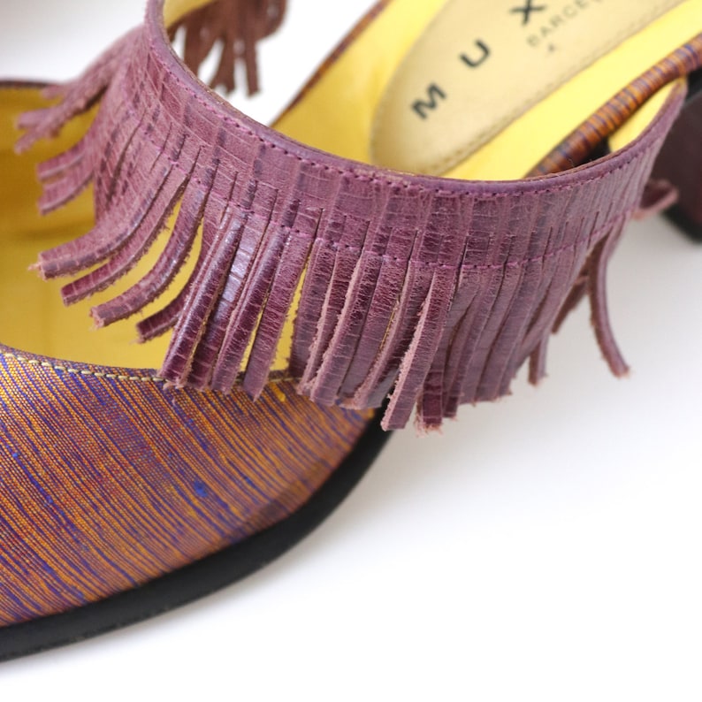 K&ouml;nnte beinhalten: Lilafarbener Lederfransen-Detail an einem gelb-violetten gemusterten Schuh mit dem Text "MUX BARCELONA" auf der Innensohle.