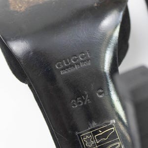 May include: Close-up of a black Gucci high heel shoe sole. The sole is marked with "GUCCI made in italy" and size "35 1/2 C". The shoe has a suede upper.