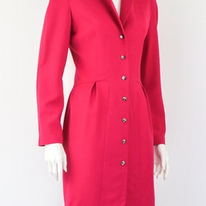 May include: A bright pink dress with a high collar and a button-up front. The dress has a fitted bodice and a slightly flared skirt.
