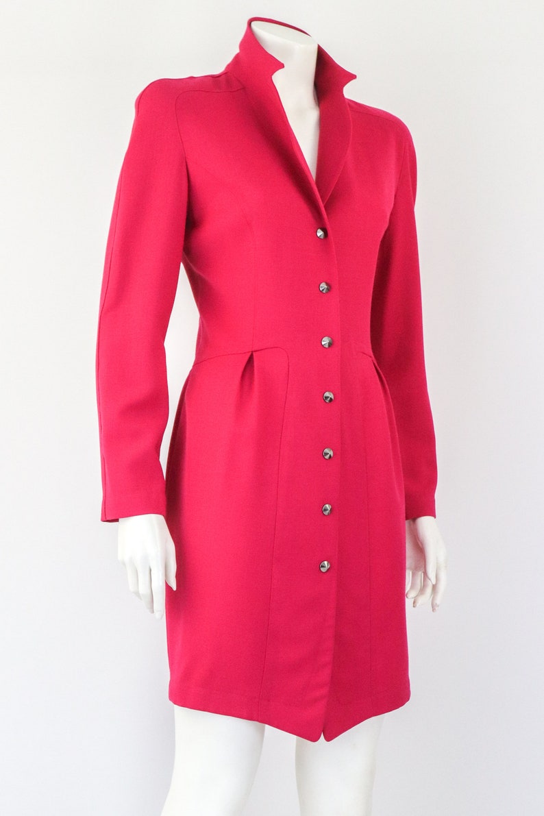 May include: A bright pink dress with a high collar and a button-up front. The dress has a fitted bodice and a slightly flared skirt.