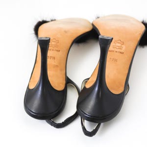 May include: A pair of black leather heeled sandals with fur trim. The sandals have a thin strap across the toes and an ankle strap. The heels are about 3 inches tall. The soles are marked "Made in Italy" and "37".