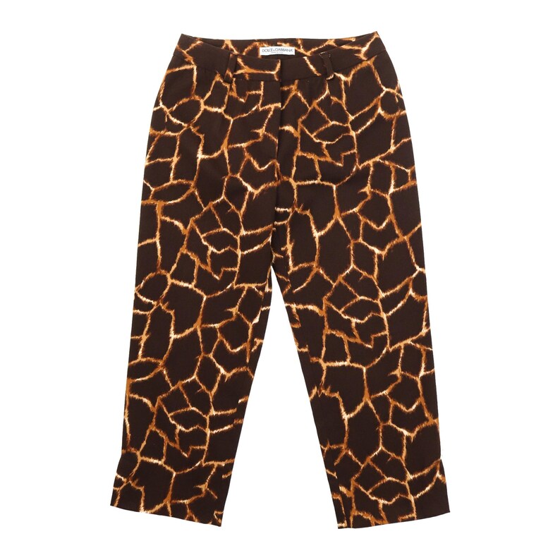 May include: Brown and tan giraffe print trousers. The trousers have a high waist and a straight leg. The fabric features a pattern of brown shapes with tan outlines. The trousers are made of a lightweight material.