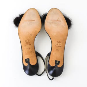 May include: Black leather heeled sandals with a black fur pom-pom on each strap. The sandals have a gold label on the sole that reads "Angelo Blassini" and "Made in Italy". The size is 37 1/2.