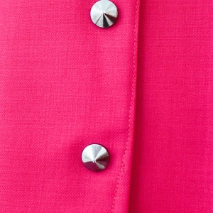 May include: Close-up of a bright pink fabric with two silver, pointed buttons.