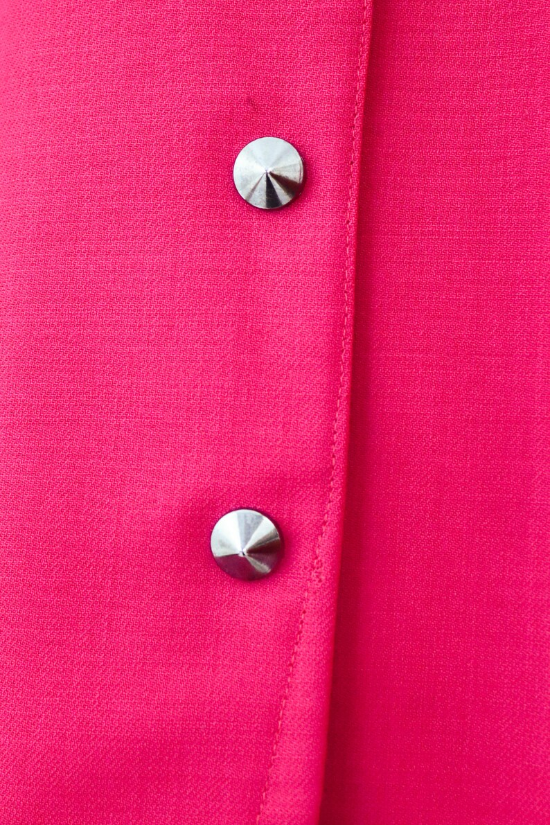 May include: Close-up of a bright pink fabric with two silver, pointed buttons.