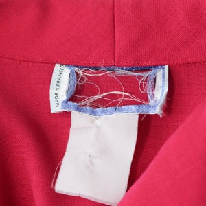May include: A close-up of a red fabric garment with a white tag that says "Made in France".