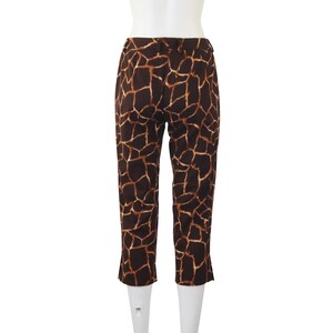 May include: Cropped trousers featuring a giraffe print in brown and tan. The back view of the trousers is displayed on a mannequin. The fabric has a repeating pattern of irregular shapes in varying shades of brown and tan.