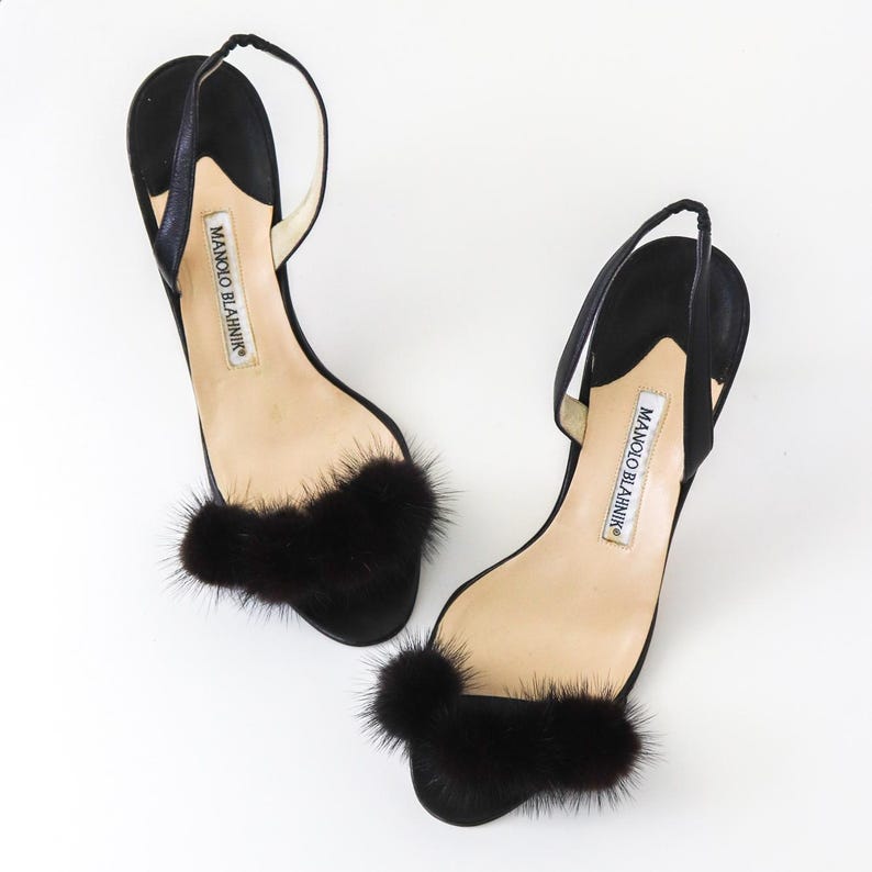 May include: A pair of black satin heeled sandals with black fur pom-poms on the toes. The sandals are by Manolo Blahnik.