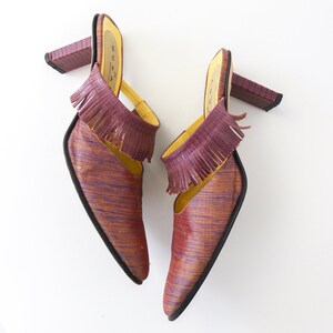 K&ouml;nnte beinhalten: Ein Paar violette und goldene Mules mit Fransen. Die Abs&auml;tze sind etwa 7,5 cm hoch.