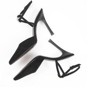 May include: A pair of black high-heeled shoes with pointed toes and ankle straps. The stiletto heels are approximately 4 inches tall. The shoes are made of a soft, suede-like material and feature delicate straps.