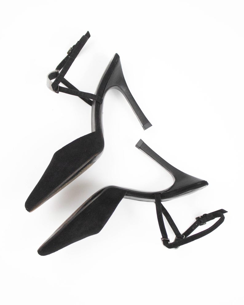 May include: A pair of black high-heeled shoes with pointed toes and ankle straps. The stiletto heels are approximately 4 inches tall. The shoes are made of a soft, suede-like material and feature delicate straps.