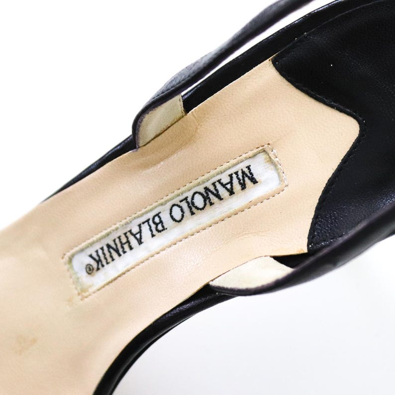 May include: Close-up of the inside of a black leather heeled shoe with a white label that reads "MANOLO BLAHNIK".