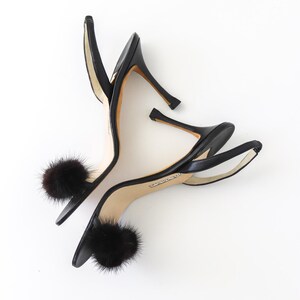 May include: A pair of black leather heeled sandals with a fur pom-pom detail on each strap.
