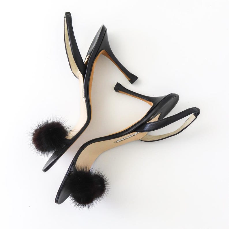 May include: A pair of black leather heeled sandals with a fur pom-pom detail on each strap.