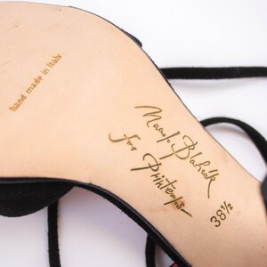 Puede incluir: Sandalia negra de ante con tac&oacute;n alto y fina correa en el tobillo. La suela es beige con letras doradas que dicen "Manolo Blahnik for Printemps" y "hand made in italy". La talla del zapato es 38 1/2.