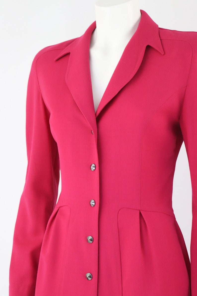 May include: A long-sleeved, pink dress with a collared neckline and button closure. The dress has a fitted bodice and a slightly flared skirt.