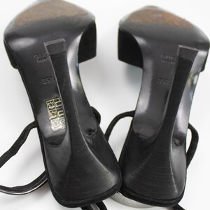 May include: A pair of black high-heeled sandals with ankle straps. The heels are slender and curved, and the soles show wear. The sandals are set against a white background, showcasing their design and details.