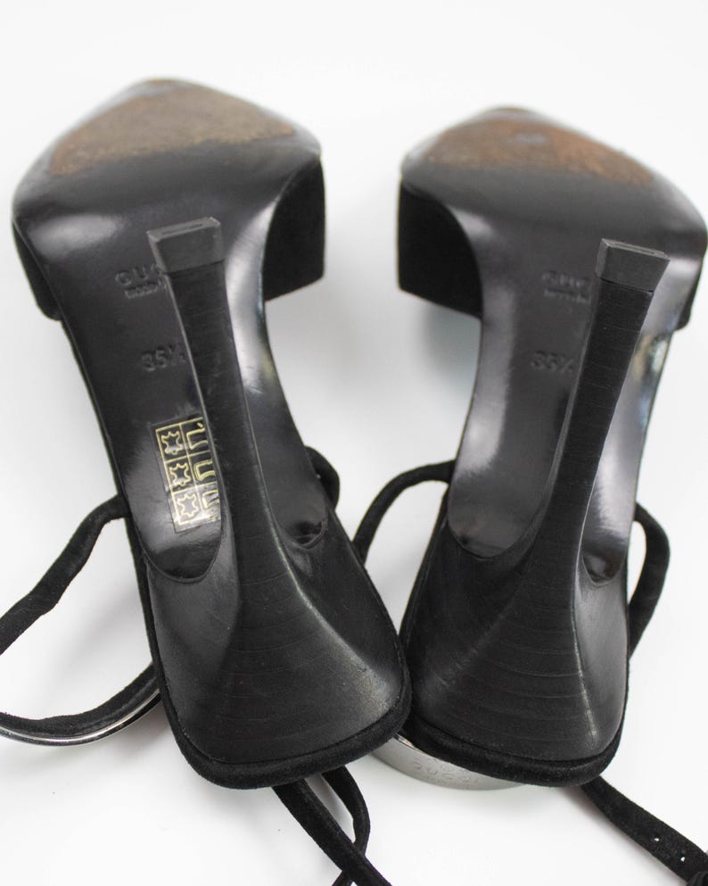 May include: A pair of black high-heeled sandals with ankle straps. The heels are slender and curved, and the soles show wear. The sandals are set against a white background, showcasing their design and details.