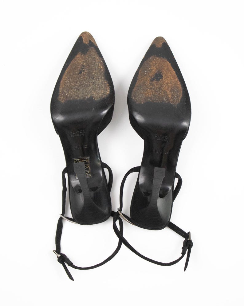 May include: Pair of black high-heeled shoes with pointed toes and ankle straps. The heels are thin and the soles show wear. The shoes are set against a white background.