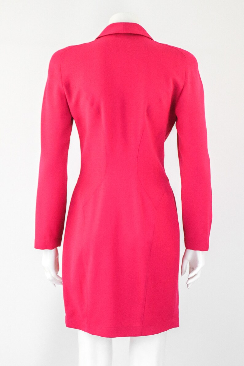 May include: A bright pink blazer with long sleeves and a single button closure. The blazer is fitted and has a slightly flared skirt.