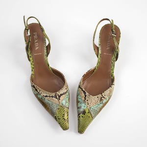 Könnte beinhalten: Ein Paar Prada Slingback-Heels mit Schlangenmuster in Grün-, Braun- und Blautönen. Die Absätze haben spitze Zehen und dünne Riemen. Das Prada-Logo ist auf der Innensohle sichtbar.