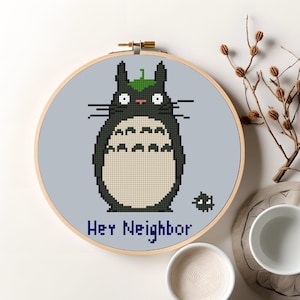 May include: A black and white cross-stitch embroidery hoop with a cartoon image of Totoro from the movie My Neighbor Totoro. The text "Hey Neighbor" is below the image.