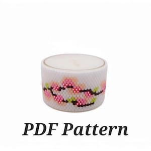 May include: White candle with a pink and green floral design on the side. The candle is in a clear glass jar with a white lid. The text "PDF Pattern" is below the candle.