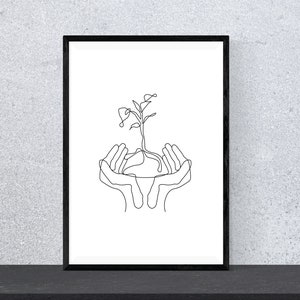 May include: A black and white line drawing of two hands cupping a small plant with roots. The image is framed in a black frame and is hanging on a gray wall.